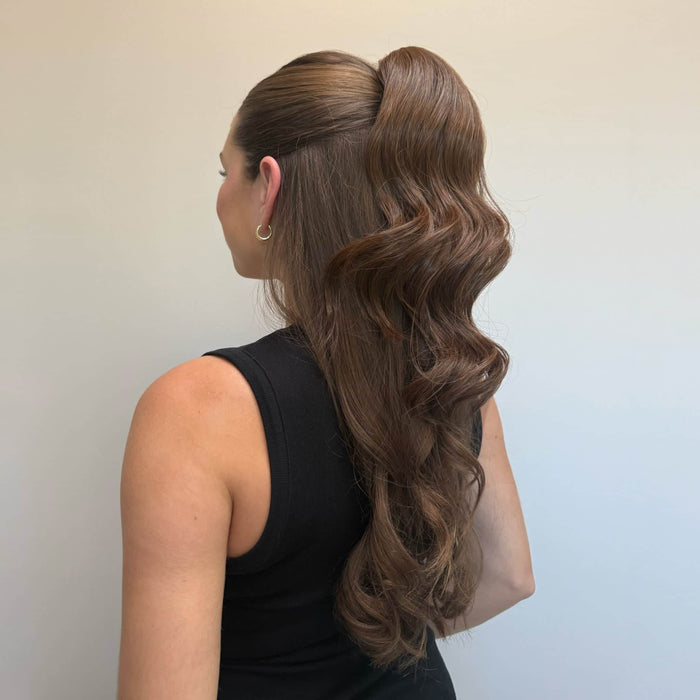 Woman with long, wavy hair styled in a ponytail against a plain background