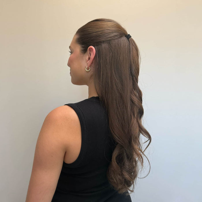 Woman with long, wavy hair styled in a ponytail against a plain background